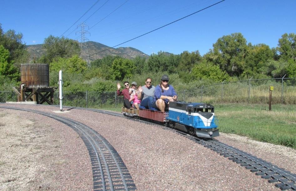 Visitors riding behind a blue locomotive on a curve with foothills in the background